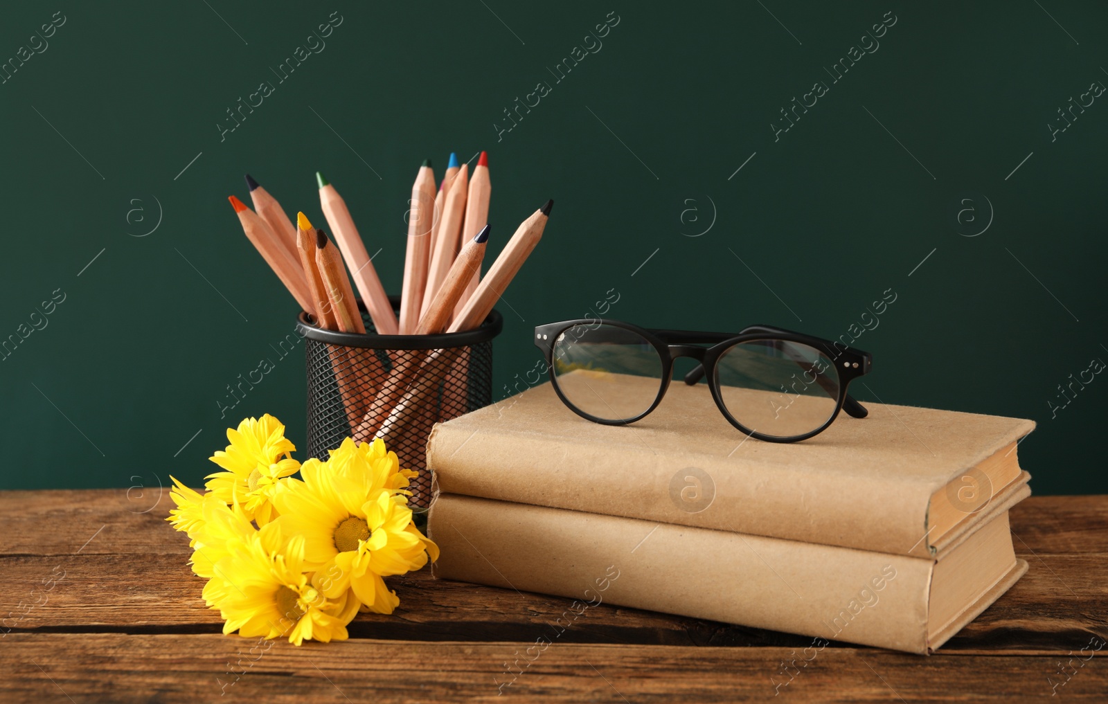 Photo of Set of stationery, glasses and flowers on wooden table near chalkboard. Teacher's Day