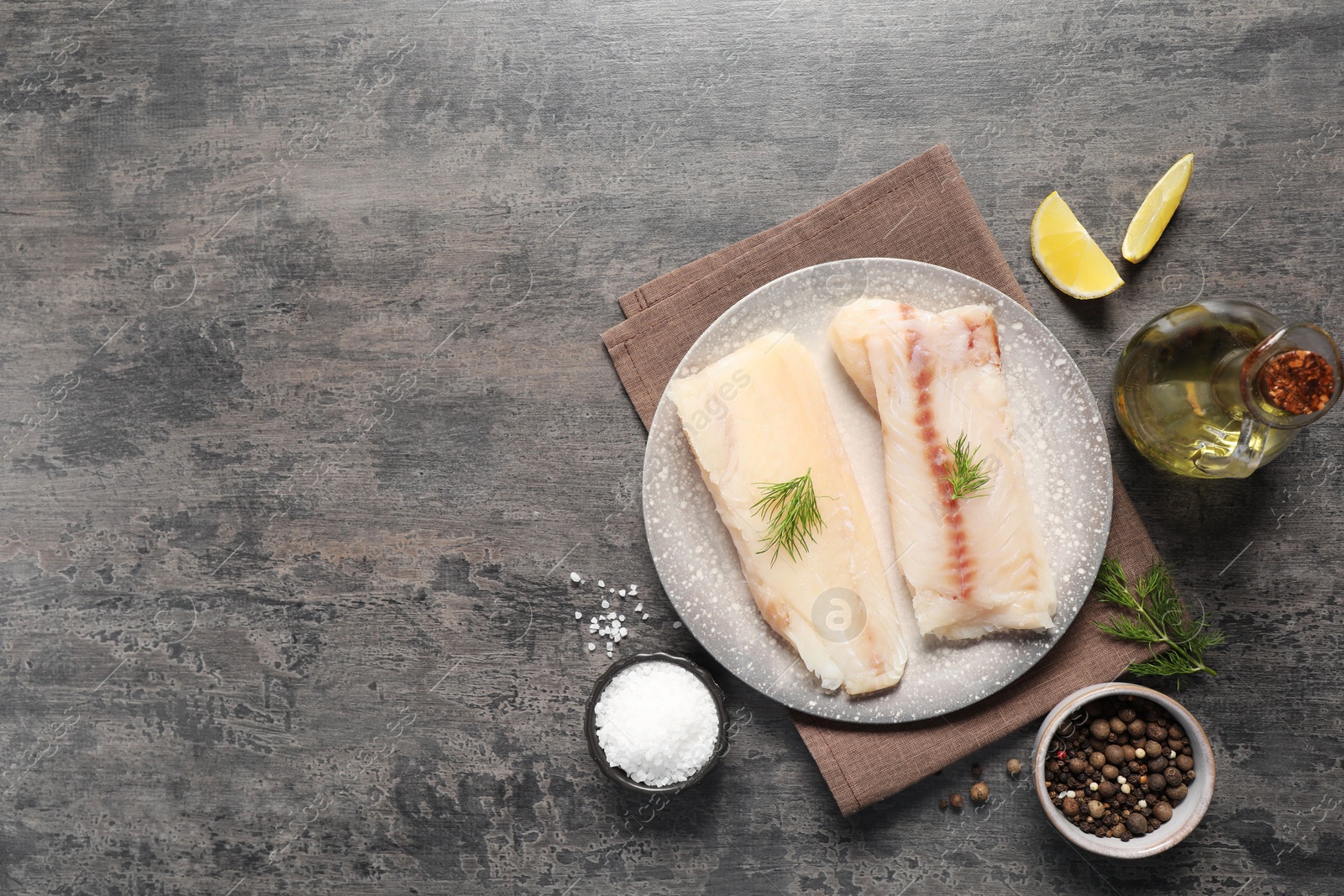 Photo of Pieces of raw cod fish, spices, oil and lemon on grey table, flat lay. Space for text