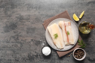 Photo of Pieces of raw cod fish, spices, oil and lemon on grey table, flat lay. Space for text