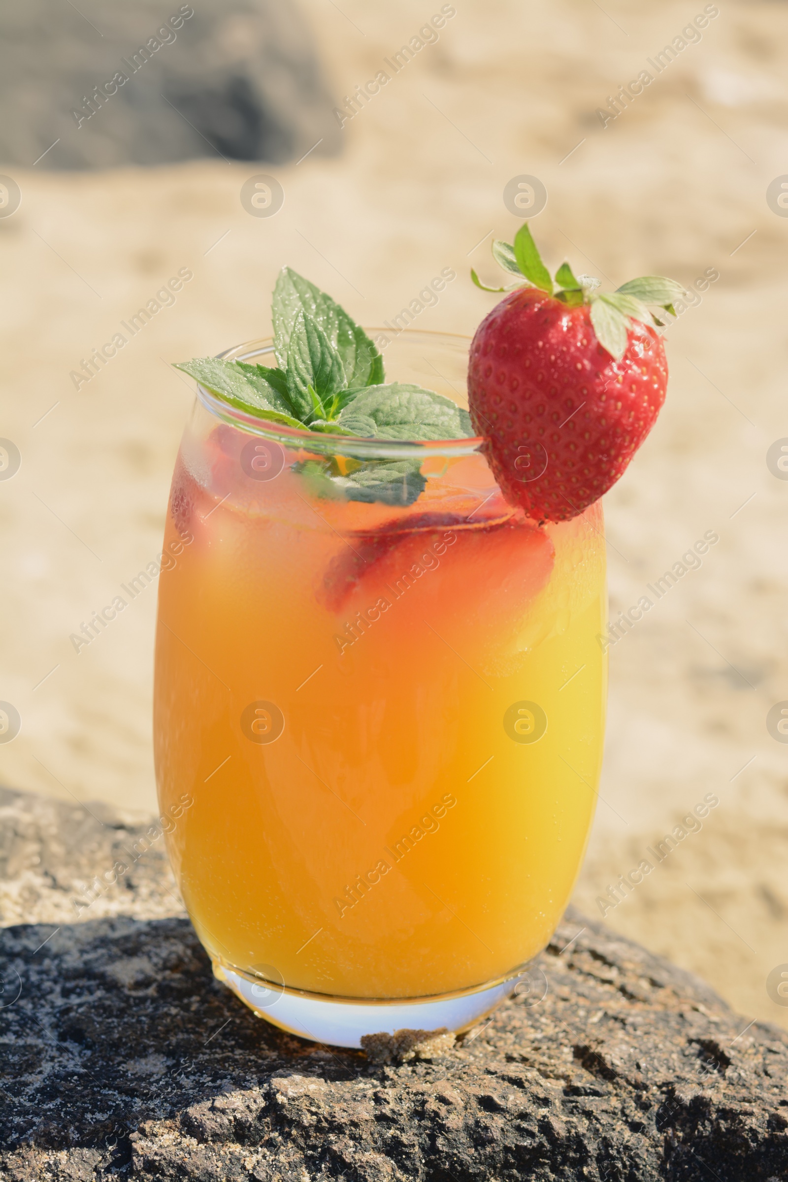 Photo of Glass of refreshing drink with strawberry and mint on rock outdoors