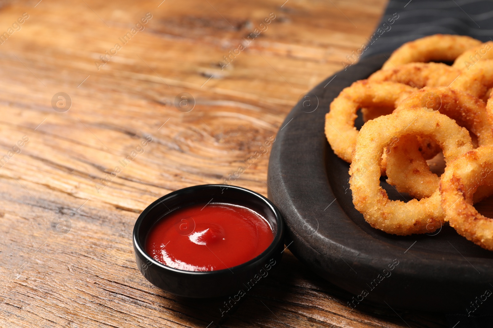 Photo of Tasty ketchup and onion rings on wooden table, closeup. Space for text