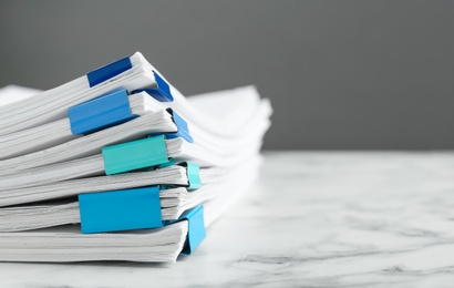 Stack of documents with binder clips on marble table against grey background, closeup. Space for text