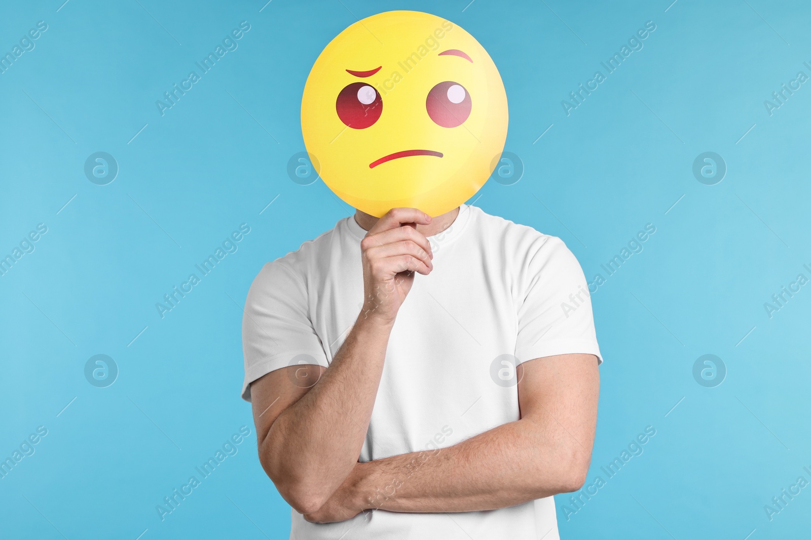 Photo of Man covering face with thinking emoticon on light blue background