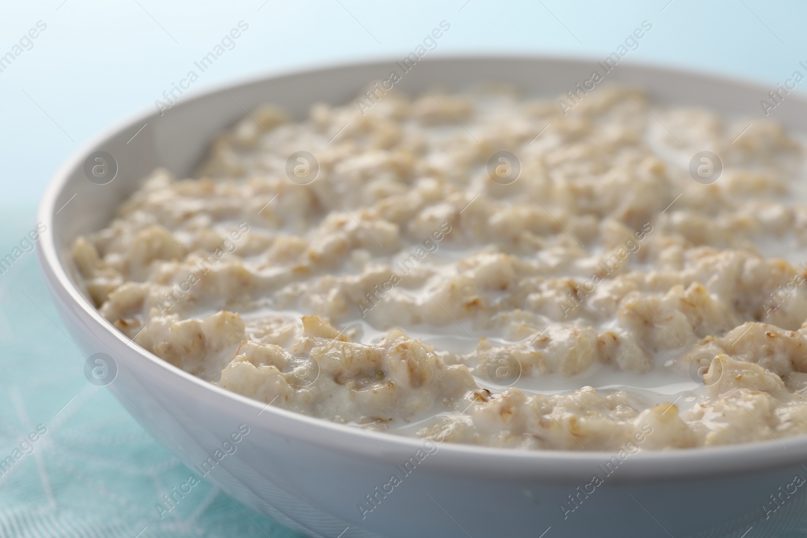 Photo of Tasty boiled oatmeal in bowl on light blue table, closeup