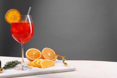 Glass of tasty Aperol spritz cocktail with orange slices and rosemary on white table against gray background, space for text