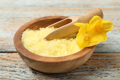 Photo of Yellow sea salt in bowl, scoop and flower on wooden table, closeup