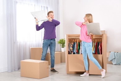 Photo of Young couple having pillow fight near wardrobe boxes at home