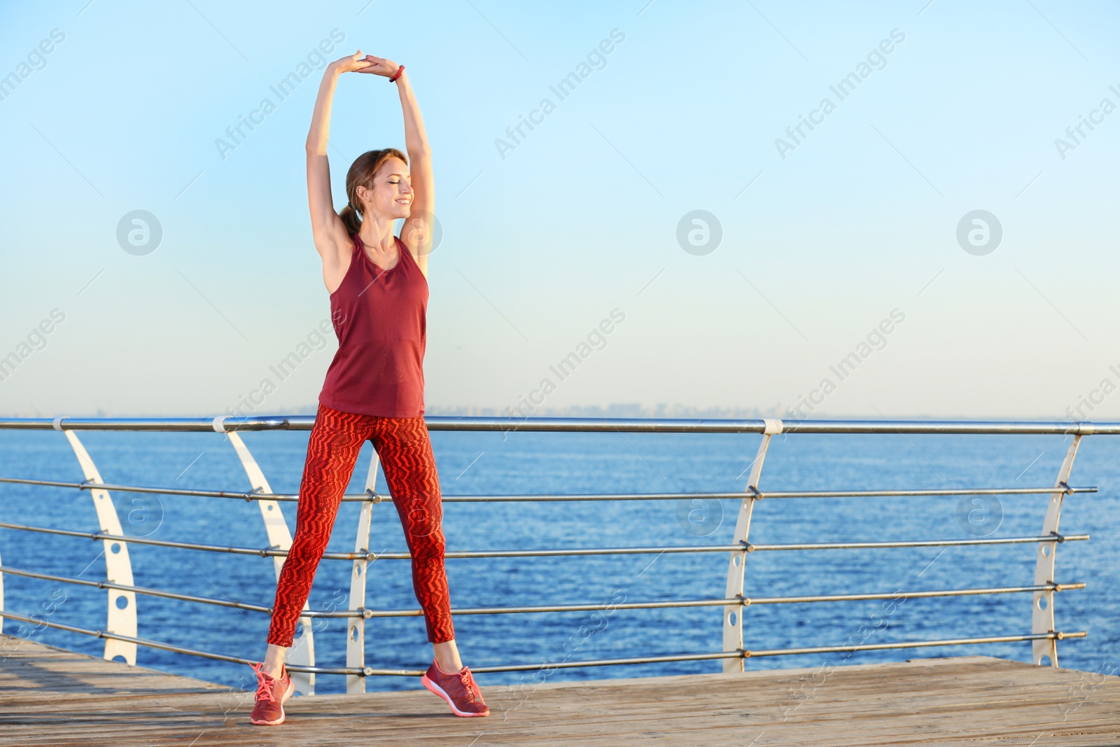 Photo of Young woman doing fitness exercises on pier in morning