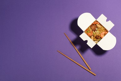 Photo of Noodle wok with chopsticks on purple background, flat lay. Space for text