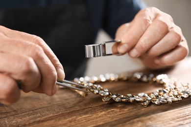 Photo of Male jeweler evaluating necklace at table in workshop, closeup