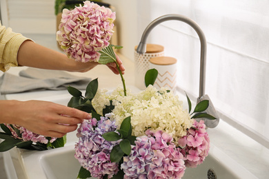 Photo of Woman making bouquet with beautiful hydrangea flowers in kitchen, closeup