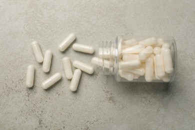 Photo of Overturned bottle with dietary supplement capsules on light grey table, flat lay