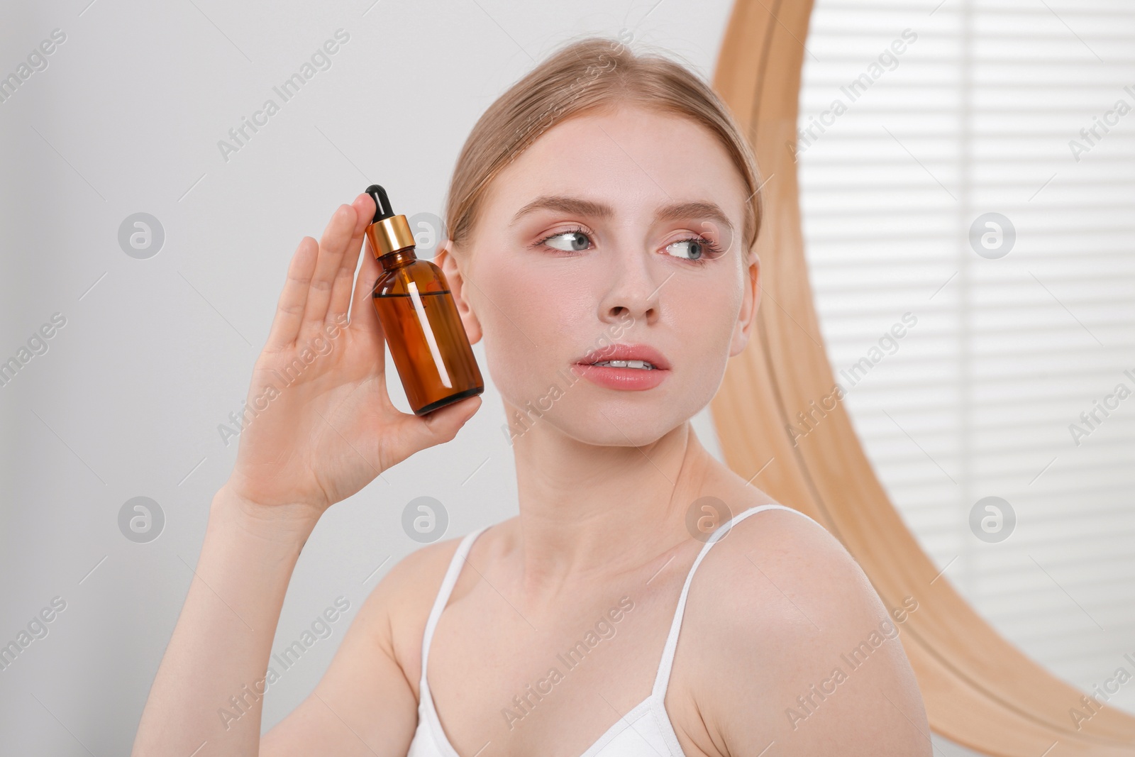 Photo of Young woman with bottle of essential oil in bathroom