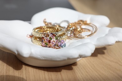 Photo of Ceramic hand stand with stylish bracelets and other accessories on wooden table, closeup