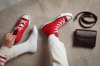 Photo of Woman with new stylish red sneakers and bag sitting on beige carpet, top view