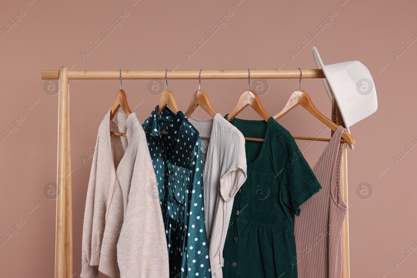 Photo of Rack with hat and stylish women`s clothes on wooden hangers against beige background