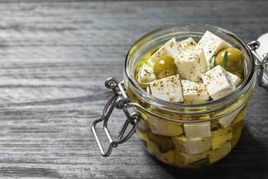 Pickled feta cheese in jar on grey wooden table, space for text