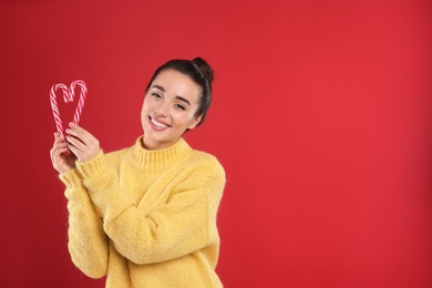 Photo of Young woman in yellow sweater holding candy canes on red background, space for text. Celebrating Christmas
