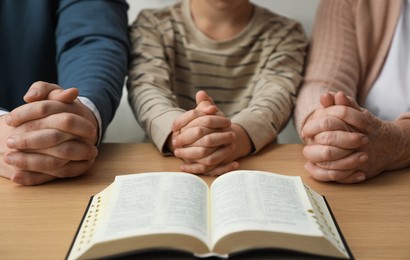 Boy and his godparents praying together at wooden table, closeup