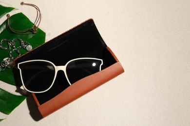 Photo of Flat lay composition with stylish sunglasses and brown leather case on sand. Space for text