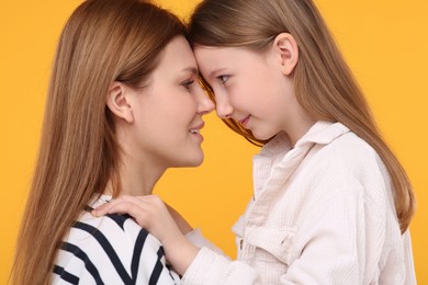 Portrait of mother and her cute daughter on orange background, closeup