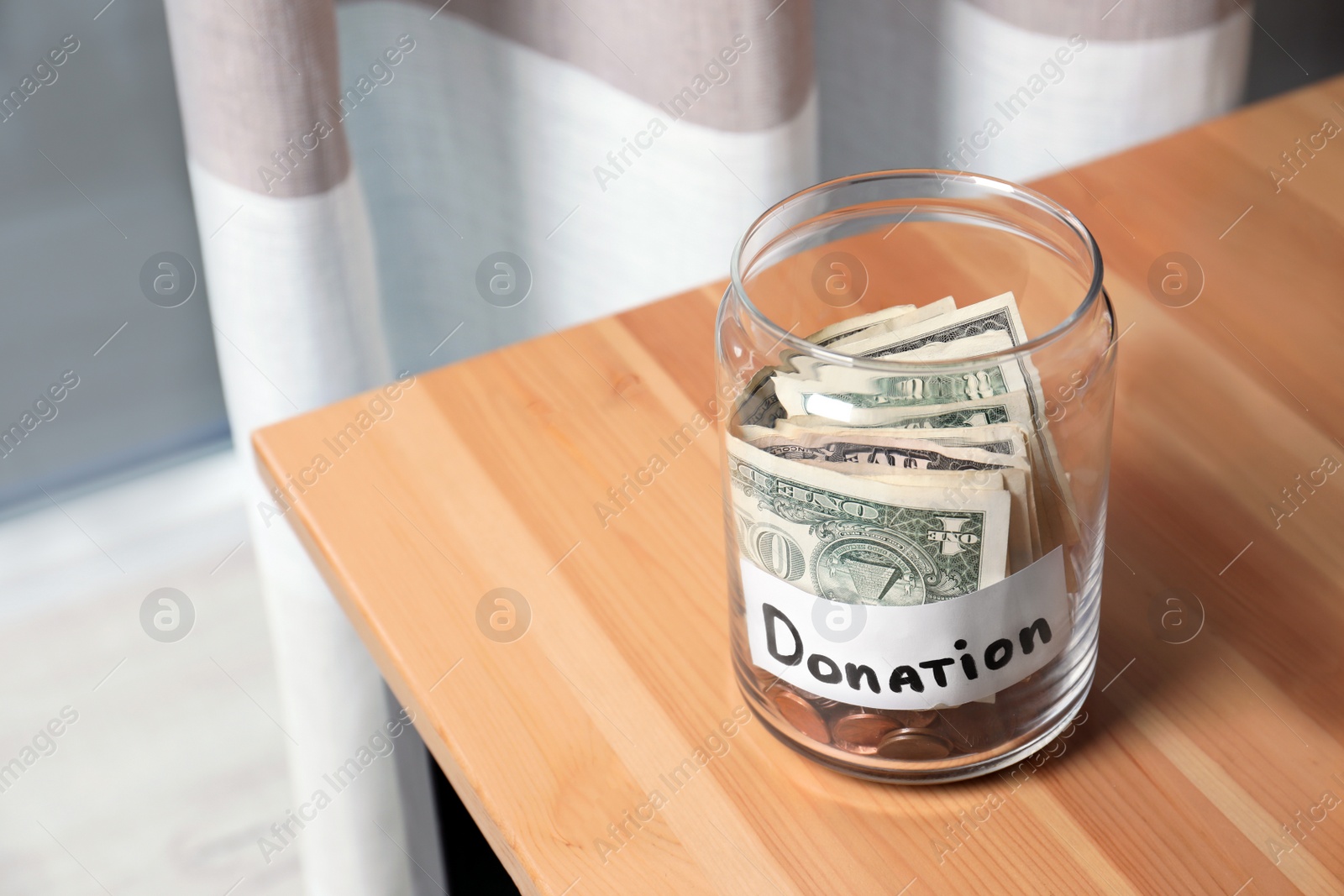 Photo of Glass jar with money and label DONATION on table against blurred background. Space for text