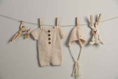 Photo of Baby clothes and accessories hanging on washing line near light grey wall