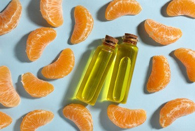 Photo of Aromatic tangerine essential oil in bottles and citrus fruits on light blue table, flat lay