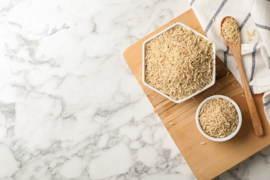 Photo of Flat lay composition with brown rice in bowls and spoon on table. Space for text