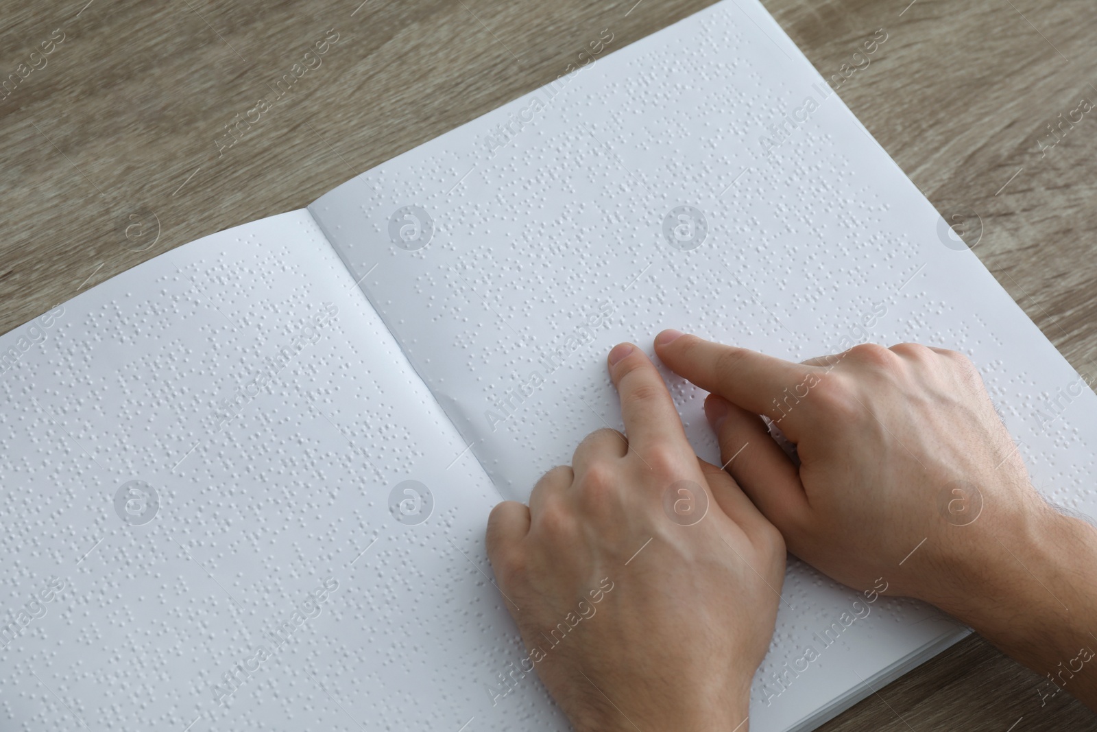 Photo of Blind man reading book written in Braille at table, closeup