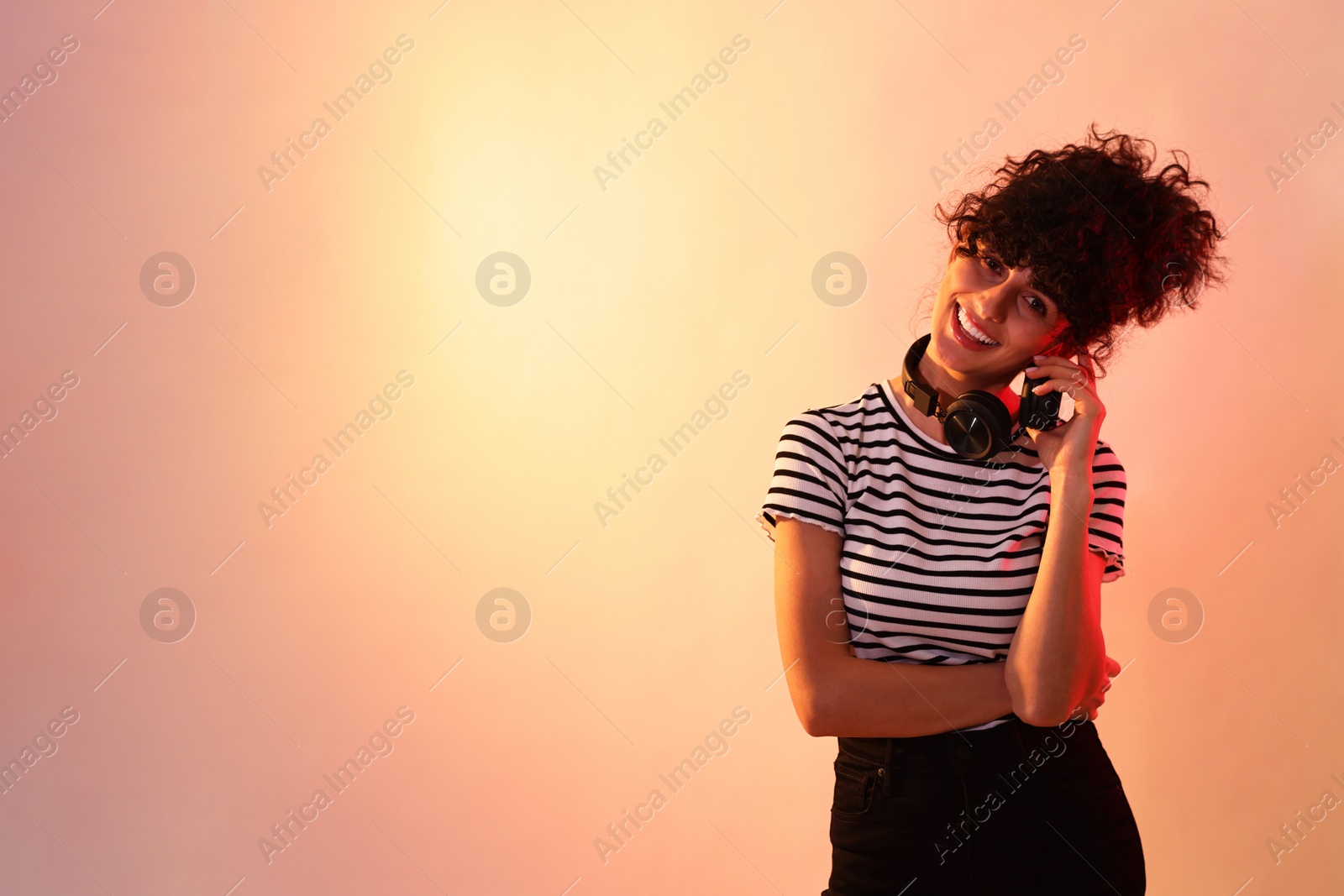 Photo of Beautiful young woman with headphones on color background in neon lights. Space for text