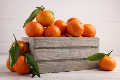 Photo of Delicious tangerines with leaves on light wooden table