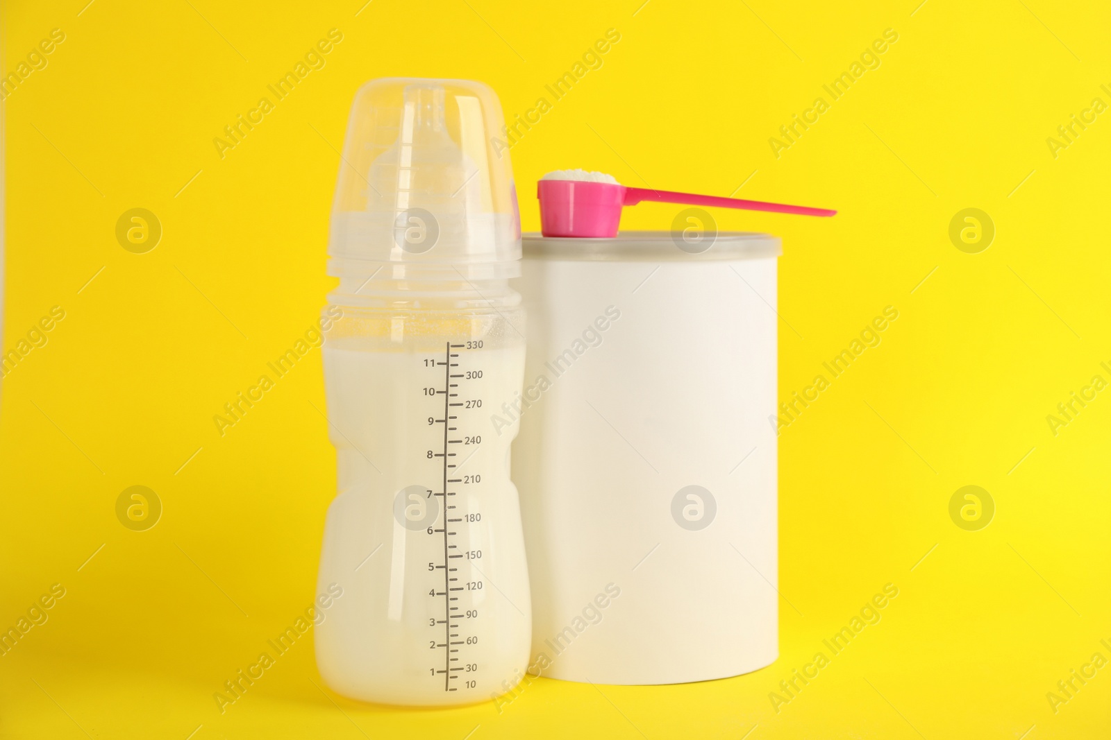 Photo of Blank can of powdered infant formula with feeding bottle and scoop on yellow background. Baby milk