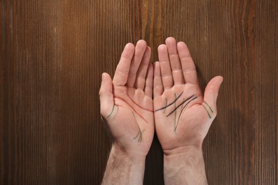 Photo of Man showing palms with drawn lines on wooden background, top view. Chiromancy and foretelling