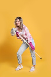 Photo of Beautiful young woman with mop singing on orange background