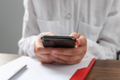 Photo of Woman using smartphone at wooden table in office, closeup