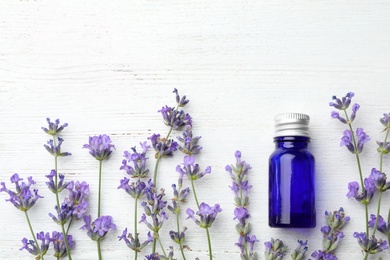 Photo of Bottle with natural essential oil and lavender flowers on white wooden background, flat lay. Space for text