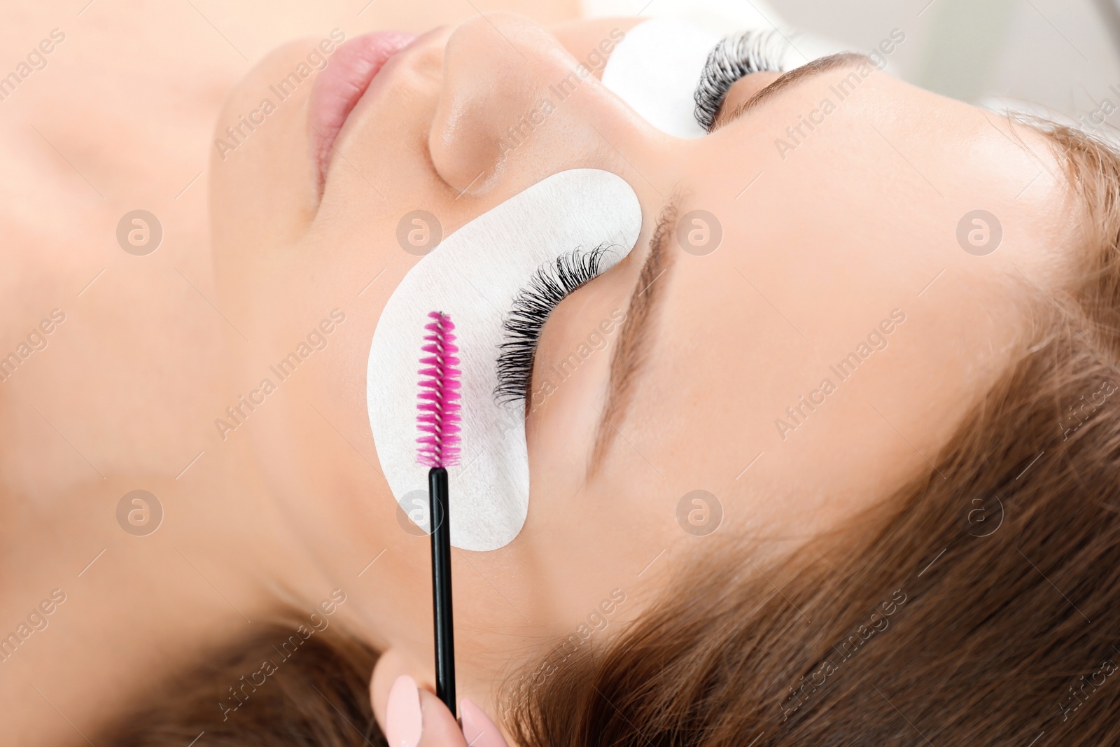 Photo of Young woman undergoing eyelash extensions procedure, closeup
