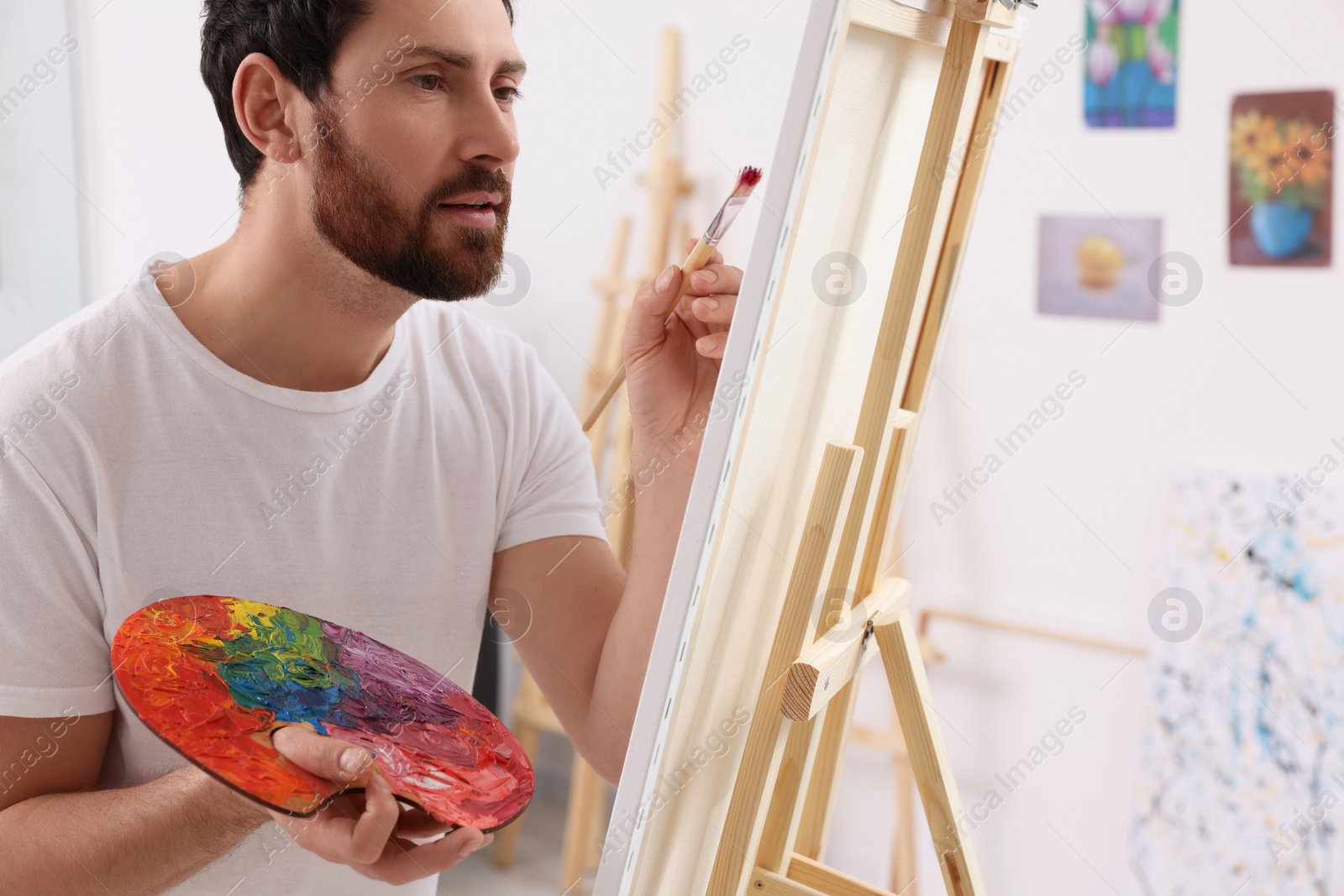 Photo of Man painting in studio. Using easel to hold canvas