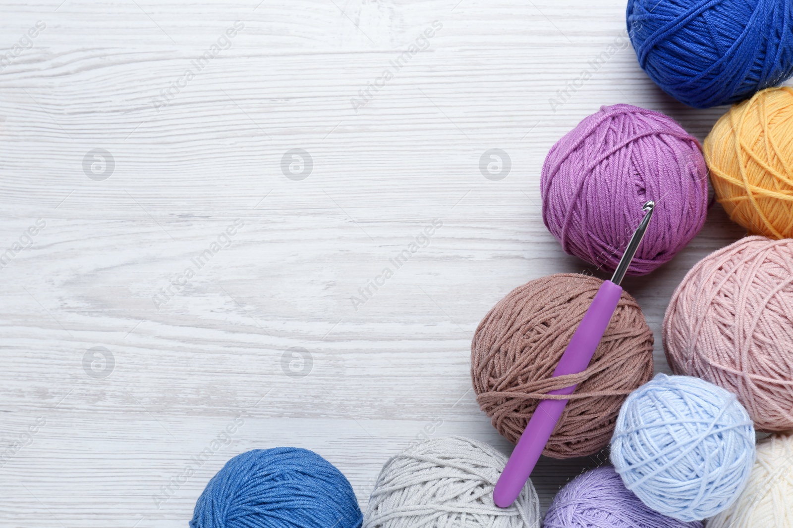 Photo of Clews of colorful knitting threads and crochet hook on white wooden table, flat lay. Space for text