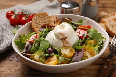 Photo of Delicious burrata salad with colorful cherry tomatoes, croutons and arugula served on wooden table