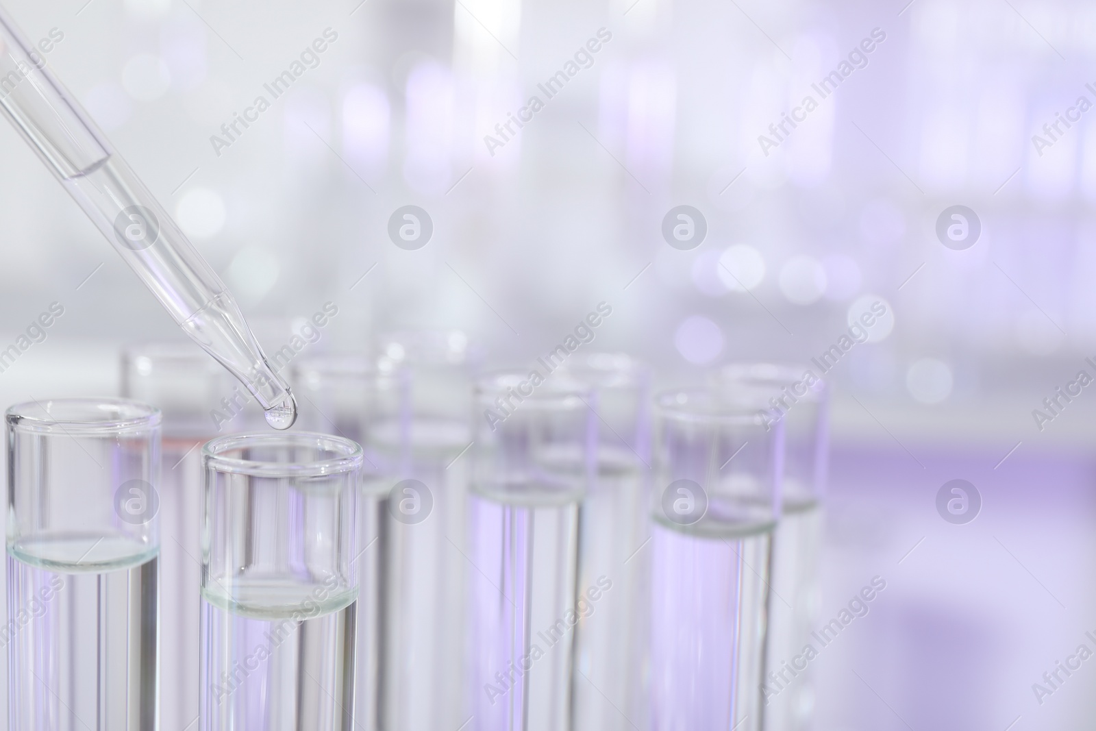 Photo of Dripping liquid from pipette into test tube on light background, closeup