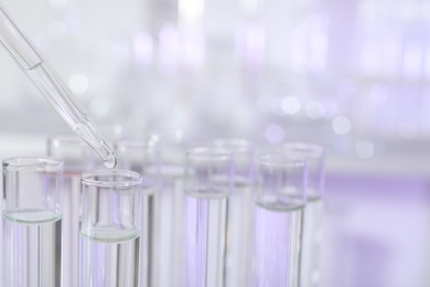 Dripping liquid from pipette into test tube on light background, closeup