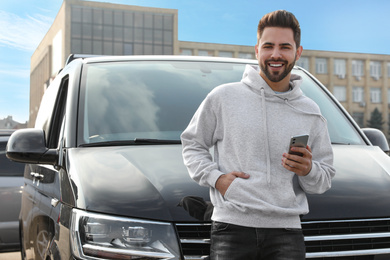 Photo of Handsome young man with smartphone near modern car outdoors