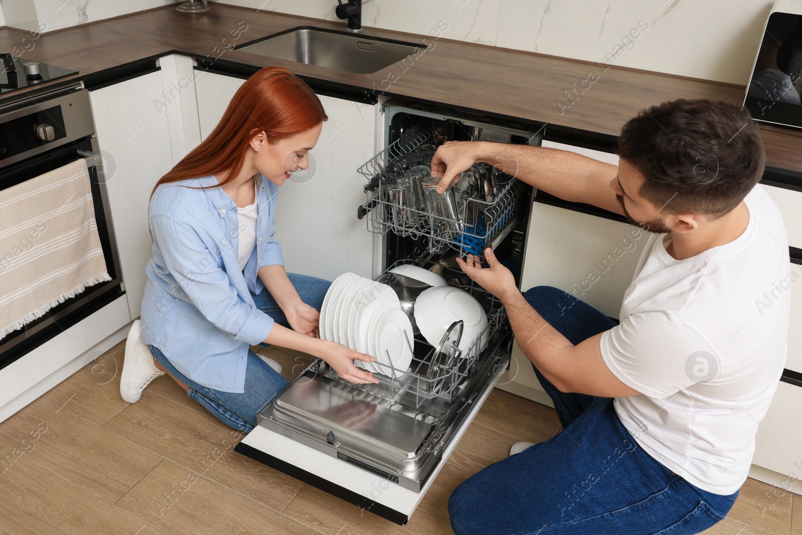 Photo of Lovely couple loading dishwasher with plates in kitchen