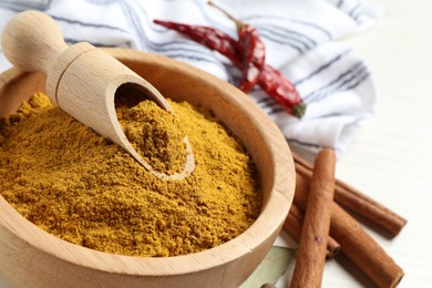 Photo of Dry curry powder in bowl and cinnamon sticks on light table, closeup