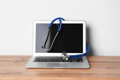 Photo of Laptop with blank screen and stethoscope on table against light background. Computer repair