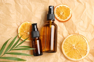 Bottles of organic cosmetic products, dried orange slices and green leaf on parchment paper, flat lay