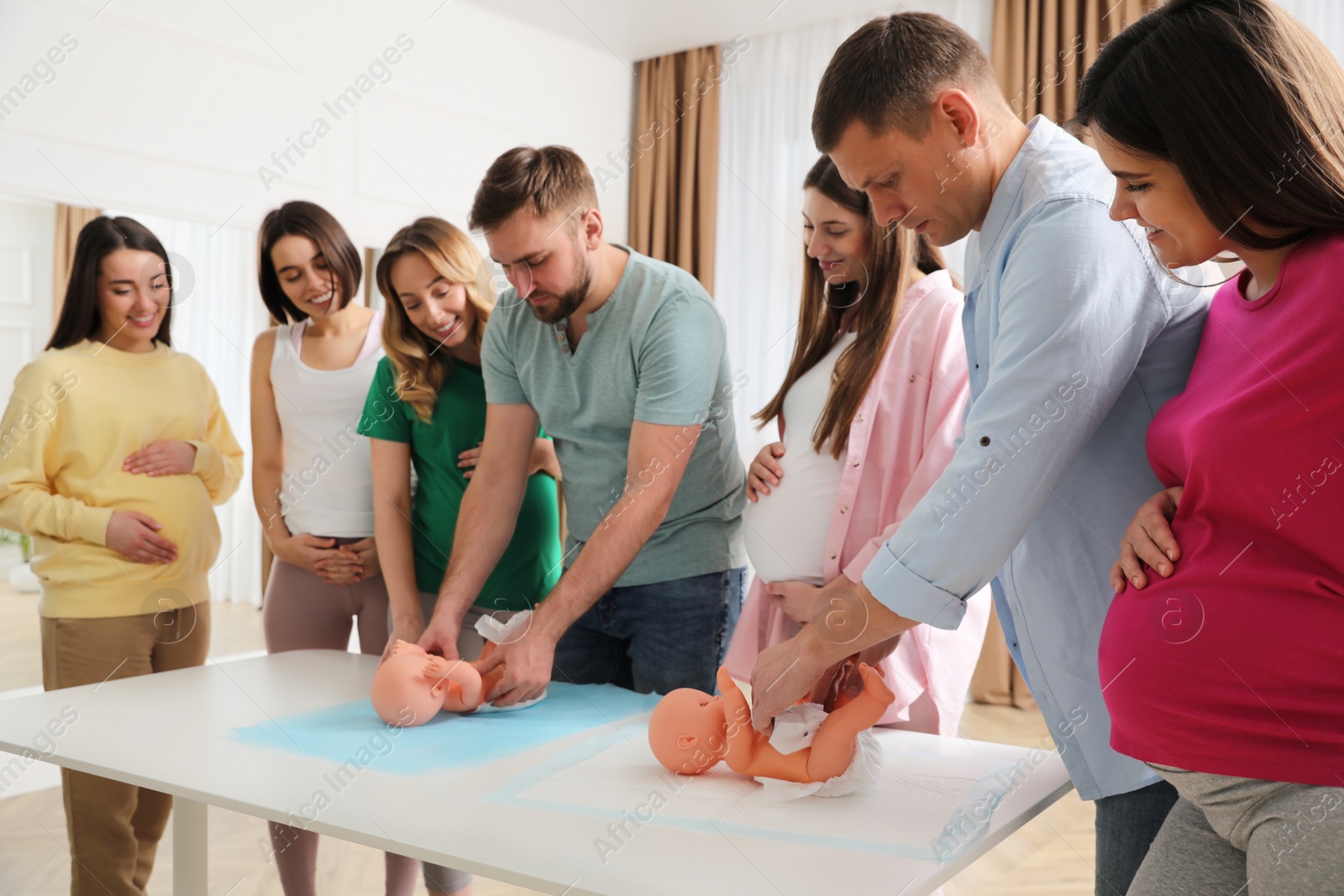 Photo of Future fathers and pregnant women learning how to swaddle baby at courses for expectant parents indoors