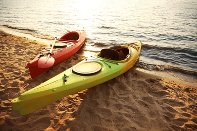 Photo of Colorful kayaks near water on river beach at sunset. Summer camp activity